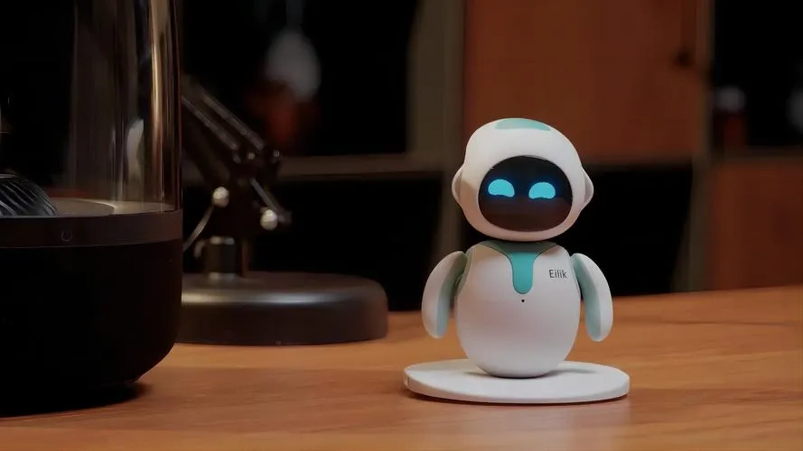 Eilik robot on a work desk next to a monitor and sticky notes